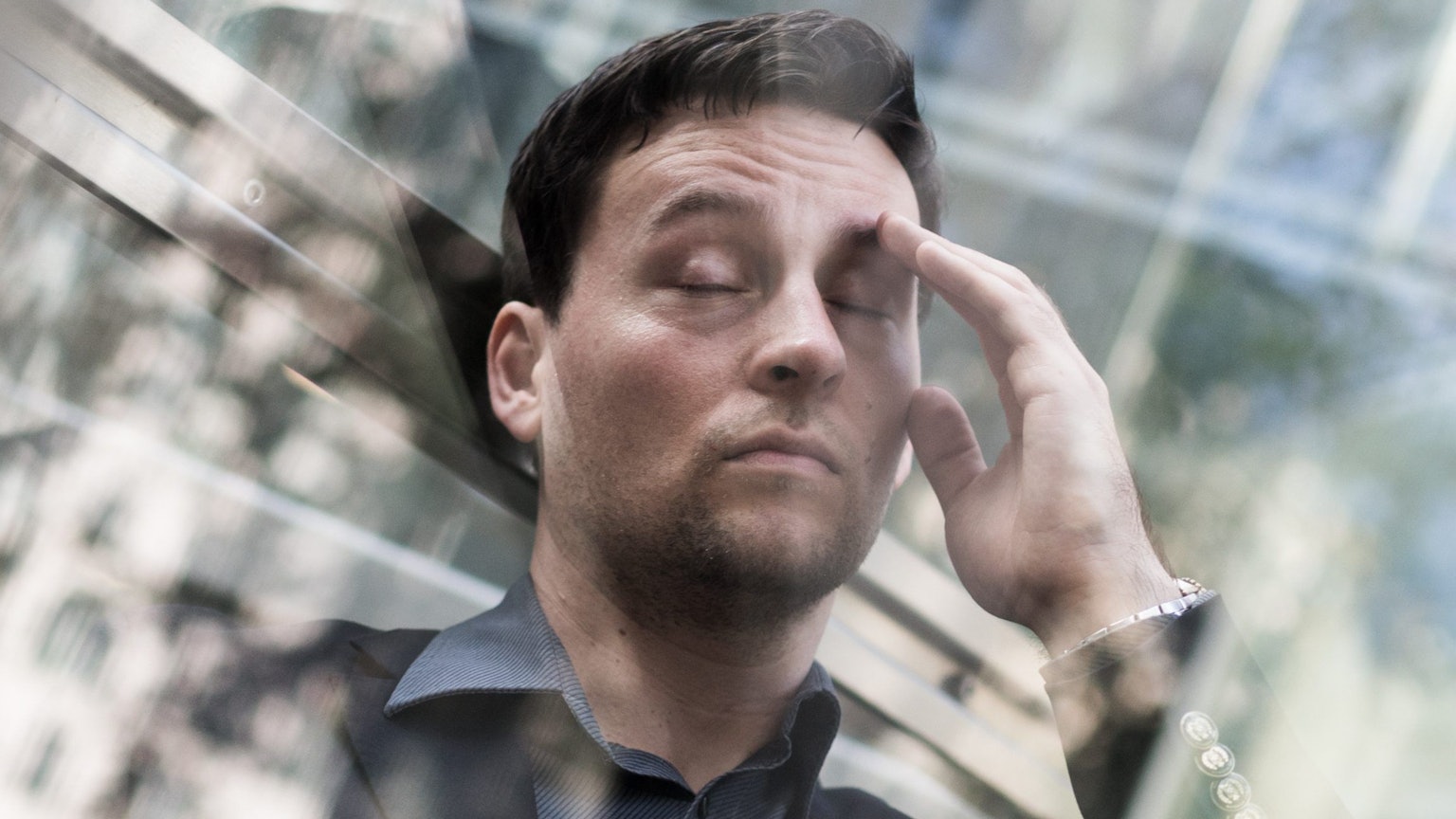 Ein Mann leidet unter Stress: Er hat die Augen geschlossen und fasst sich an den Kopf.