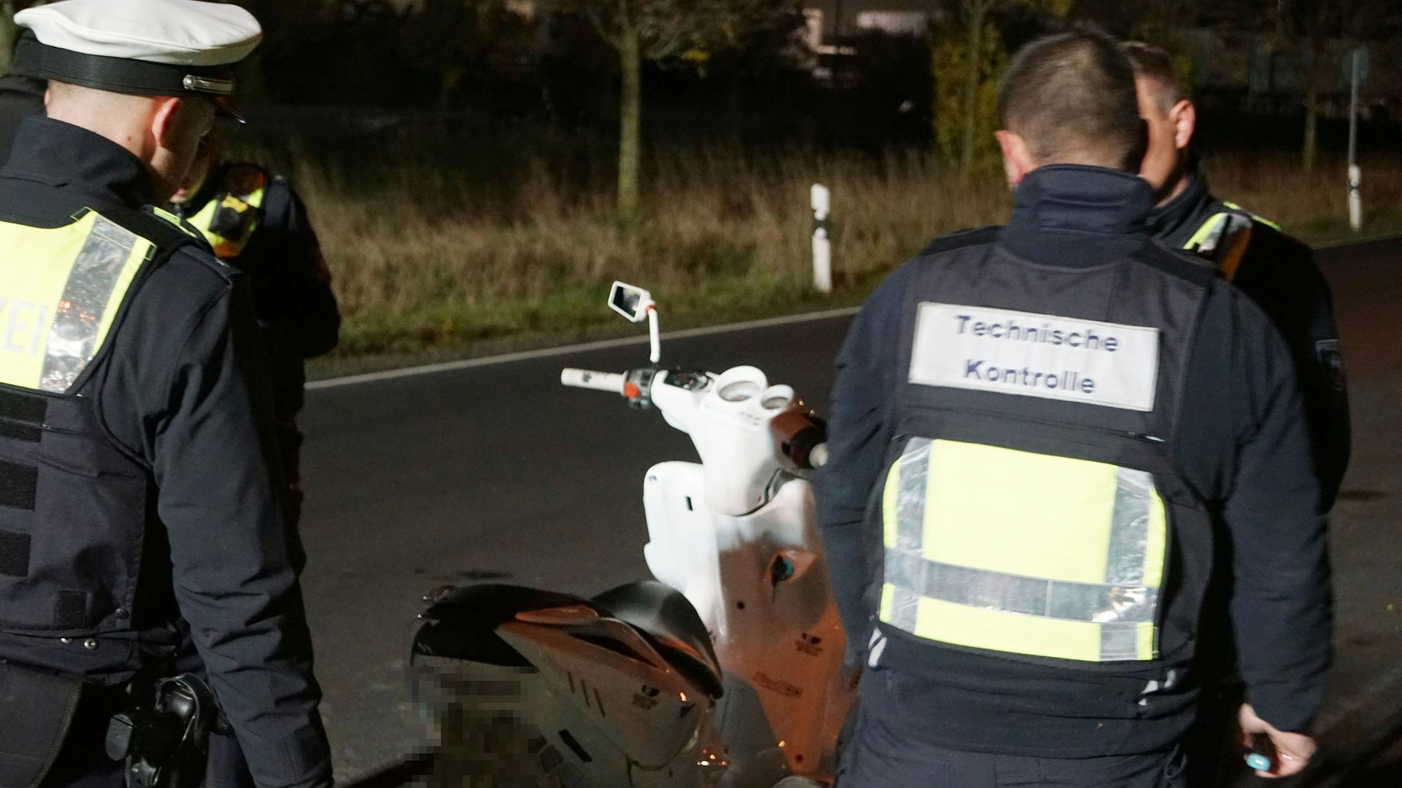 Polizisten untersuchen bei einer Verkehrskontrolle den Motorroller eines Verkehrsteilnehmers.