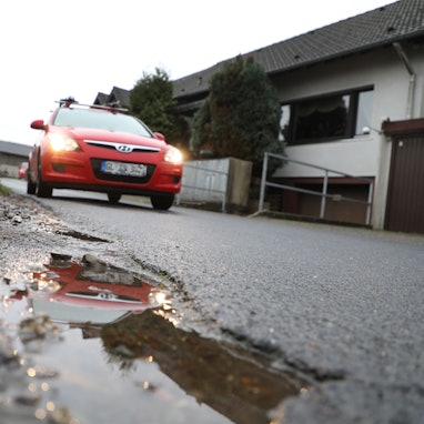 Ein Auto fährt auf einer Straße und spiegelt sich in einer Pfütze.