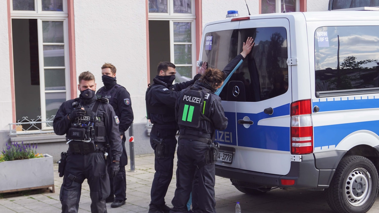 Polizisten stehen vor einem Einsatzwagen und haben eine Person in Gewahrsam genommen.