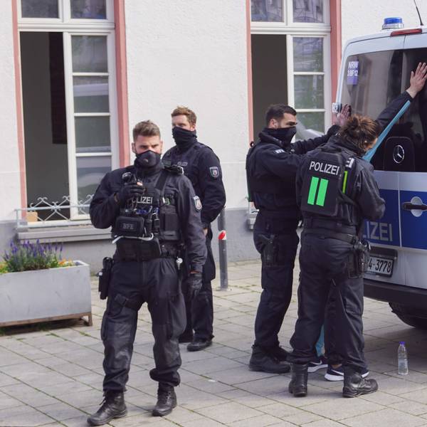Polizisten stehen vor einem Einsatzwagen und haben eine Person in Gewahrsam genommen.