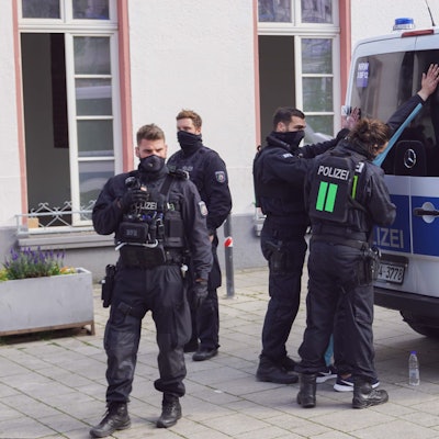 Polizisten stehen vor einem Einsatzwagen und haben eine Person in Gewahrsam genommen.