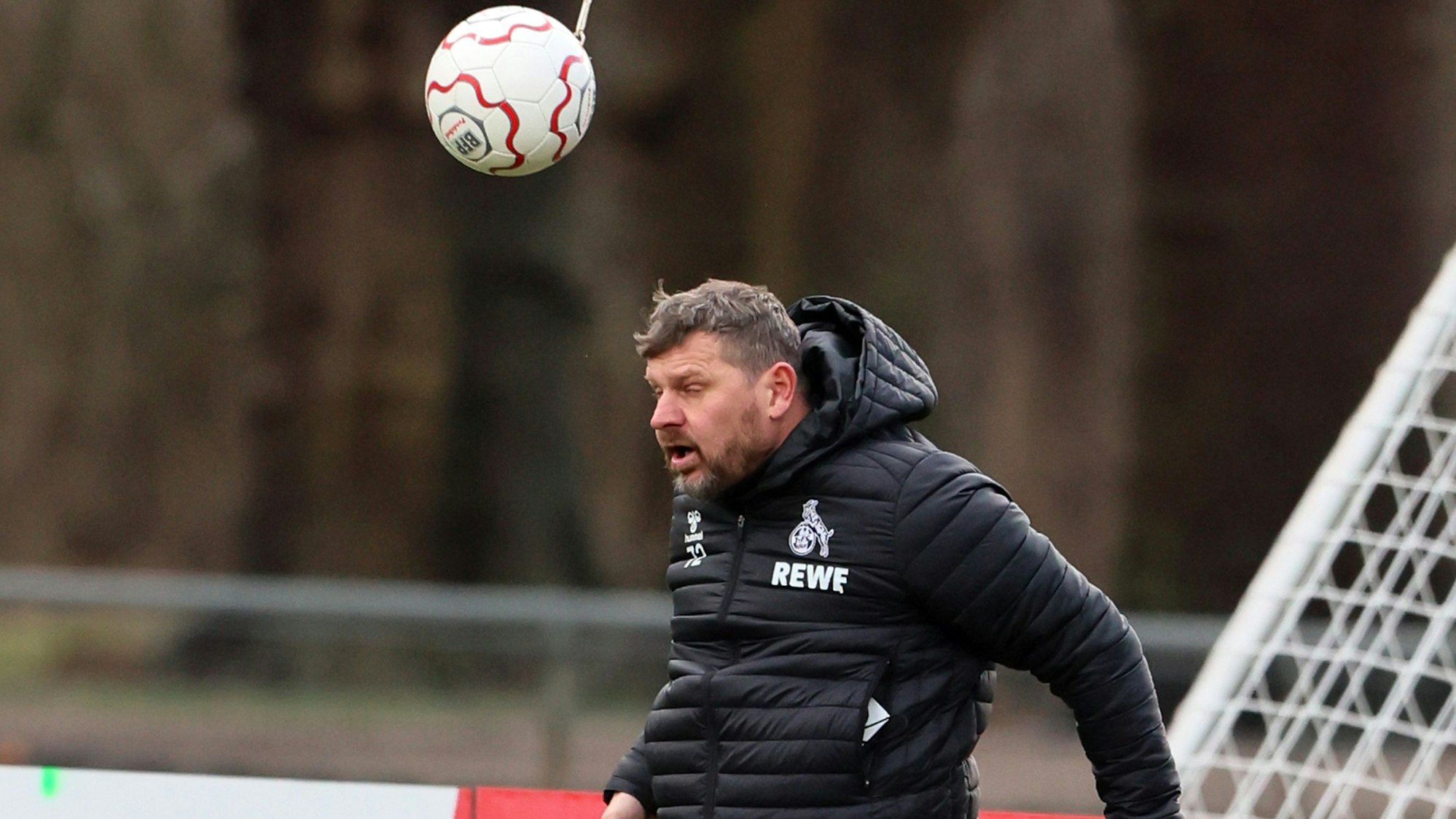 Steffen Baumgart, Trainer des 1. FC Köln, springt auf dem Trainingsplatz nach einem Ball, der am Kopfballpendel befestigt ist. Der ehemalige Stürmer hat die Augen geschlossen und erwischt die Kugel.