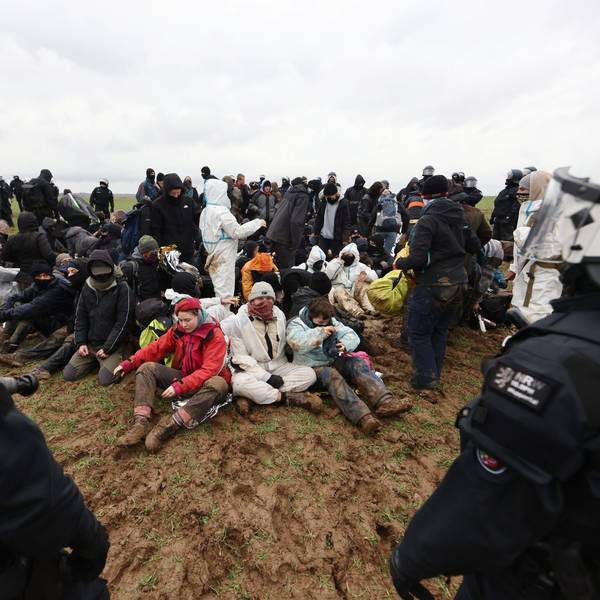 Polizisten und Klimaaktivisten auf einem Feld nahe der Abrisskante von Garzweiler II.Die Klimaschützer sitzen auf der Erde und sind von Sicherheitskräften umgeben.