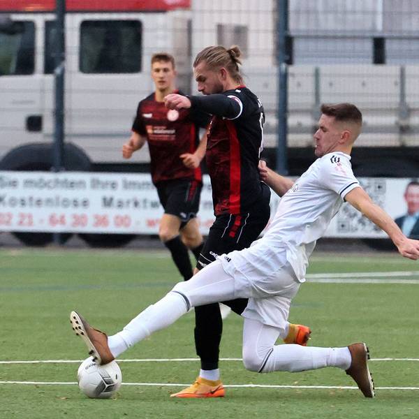 Ein Fußballspieler setzt im Zweikampf zu einer Grätsche an.