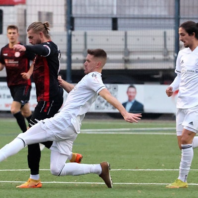 Ein Fußballspieler setzt im Zweikampf zu einer Grätsche an.