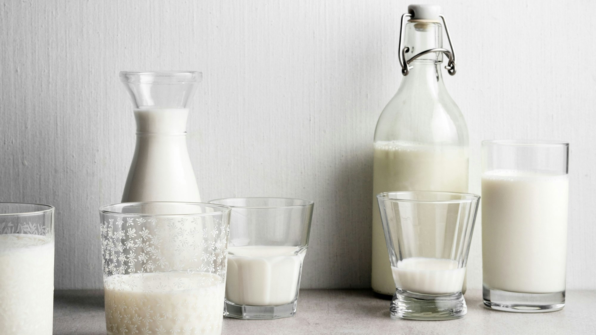 Links im Bild ist Milch in Gläsern und einer Flasche, während auf der rechten Seite Milchalternativen abgefüllt sind.