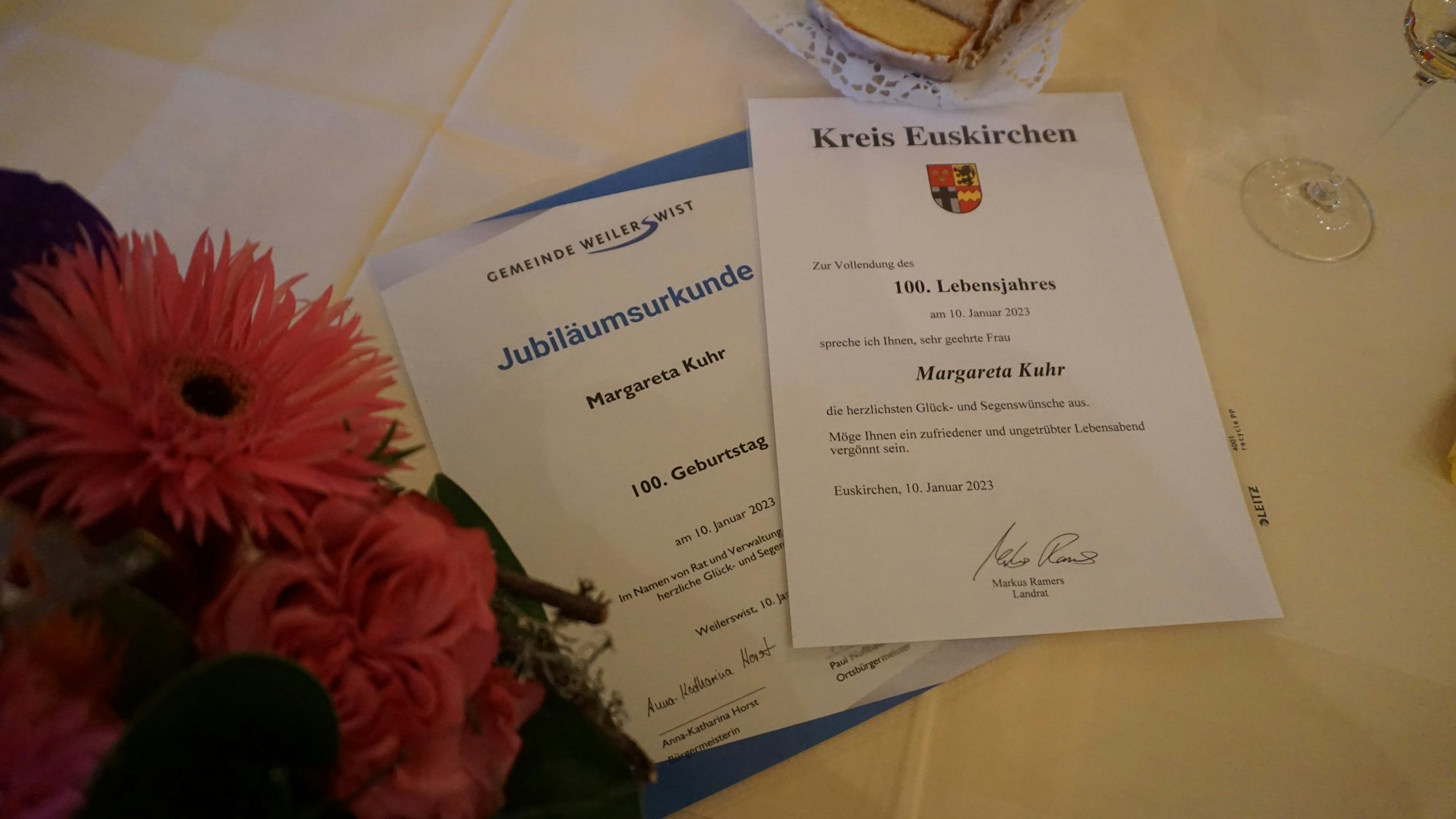 Jubiläumsurkunden des Kreis Euskirchen und der Gemeinde Weilerswist liegen auf einem Tisch neben einem Blumenstrauß.