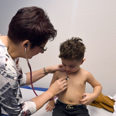 Eine Ärztin hört mit einem Stethoskop den Brustbereich eines kleinen Jungen ab.