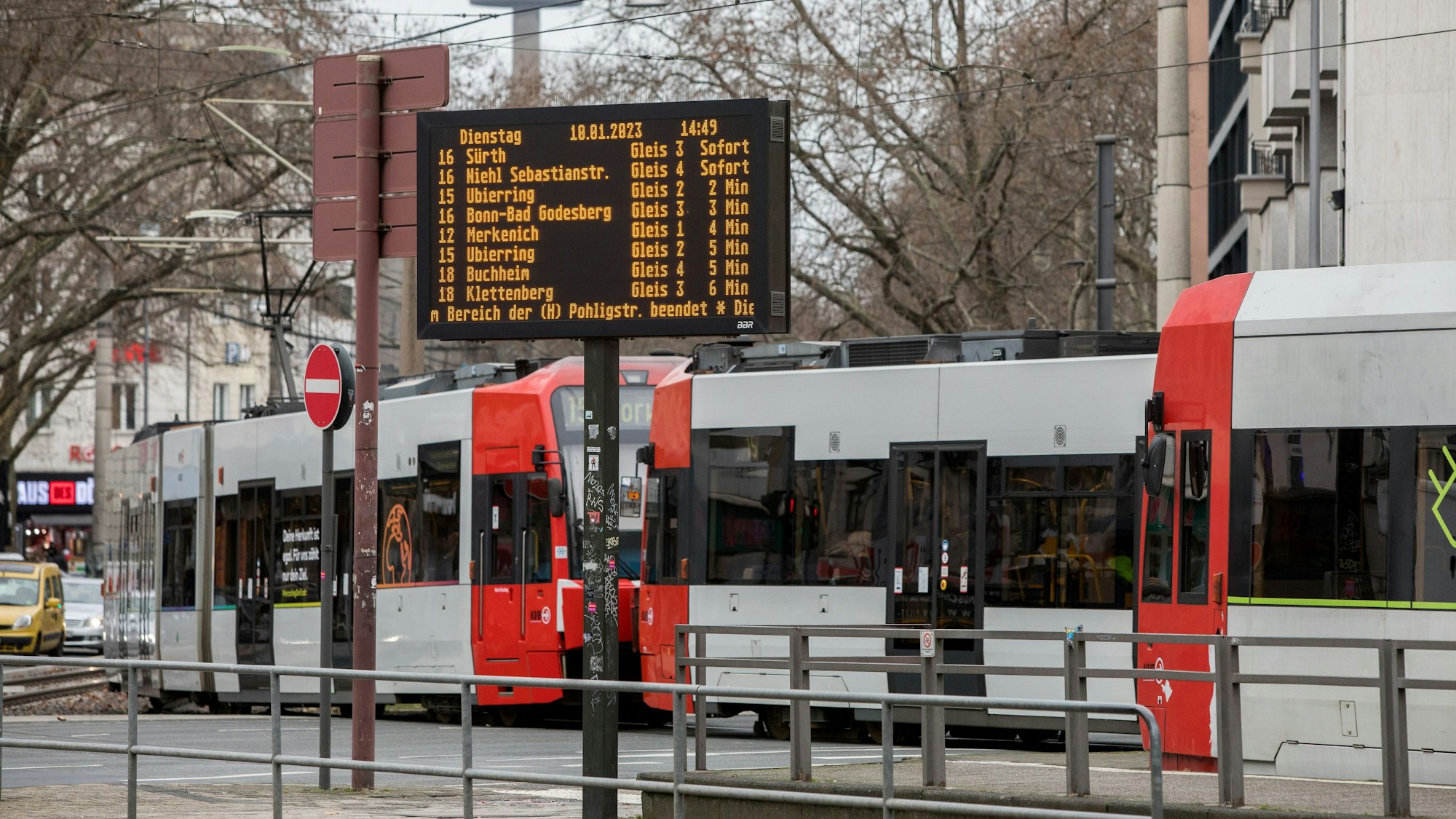 Eine Straßenbahn passiert die Haltestelle am Barbarossaplatz. Im Bildvordergrund befindet sich eine digitale Anzeigetafel mit Angaben zu den nächsten Bahnverbindungen.