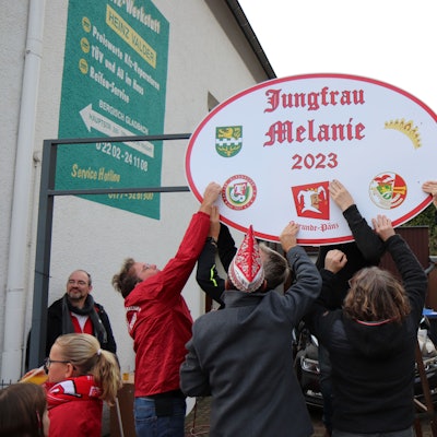 Karnevalisten bringen ein Schild mit der Aufschrift „Jungfrau Melanie 2023“ an.