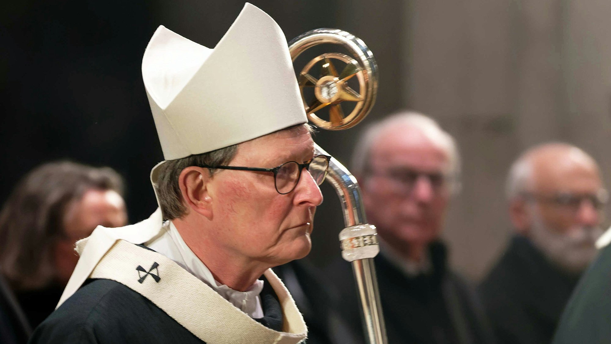 Der Kardinal Rainer Woelki zieht mit weißer Mitra, dem Bischofshut, und Hirtenstab zu einem Gedenkgottesdienst für den verstorbenen Papst Benedikt XVI. in den Kölner Dom ein. Im Hintergrund wird er von Gläubigen beobachtet.