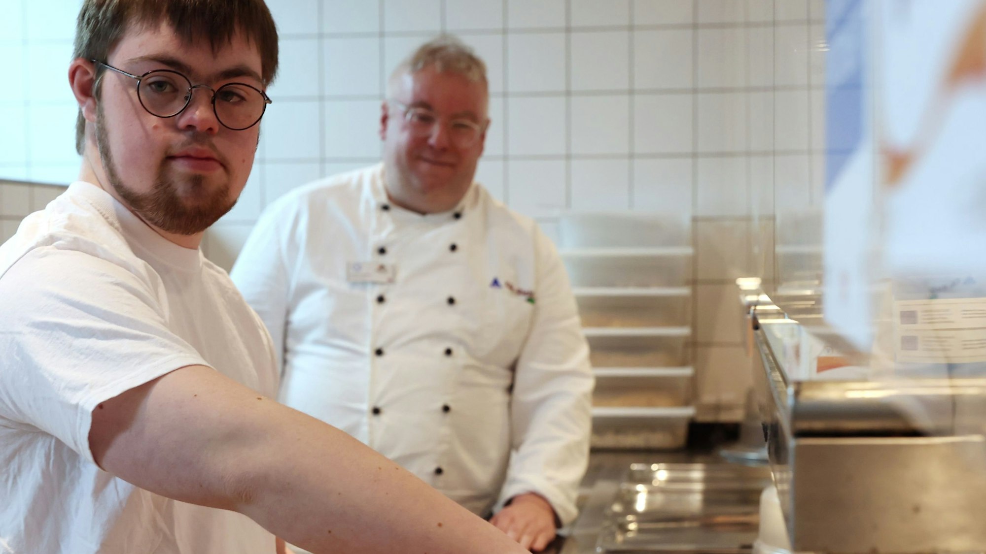 Ein junger Mann mit Brille im weißen T-Shirt füllt einen Teller mit Nudeln und Sauce.
