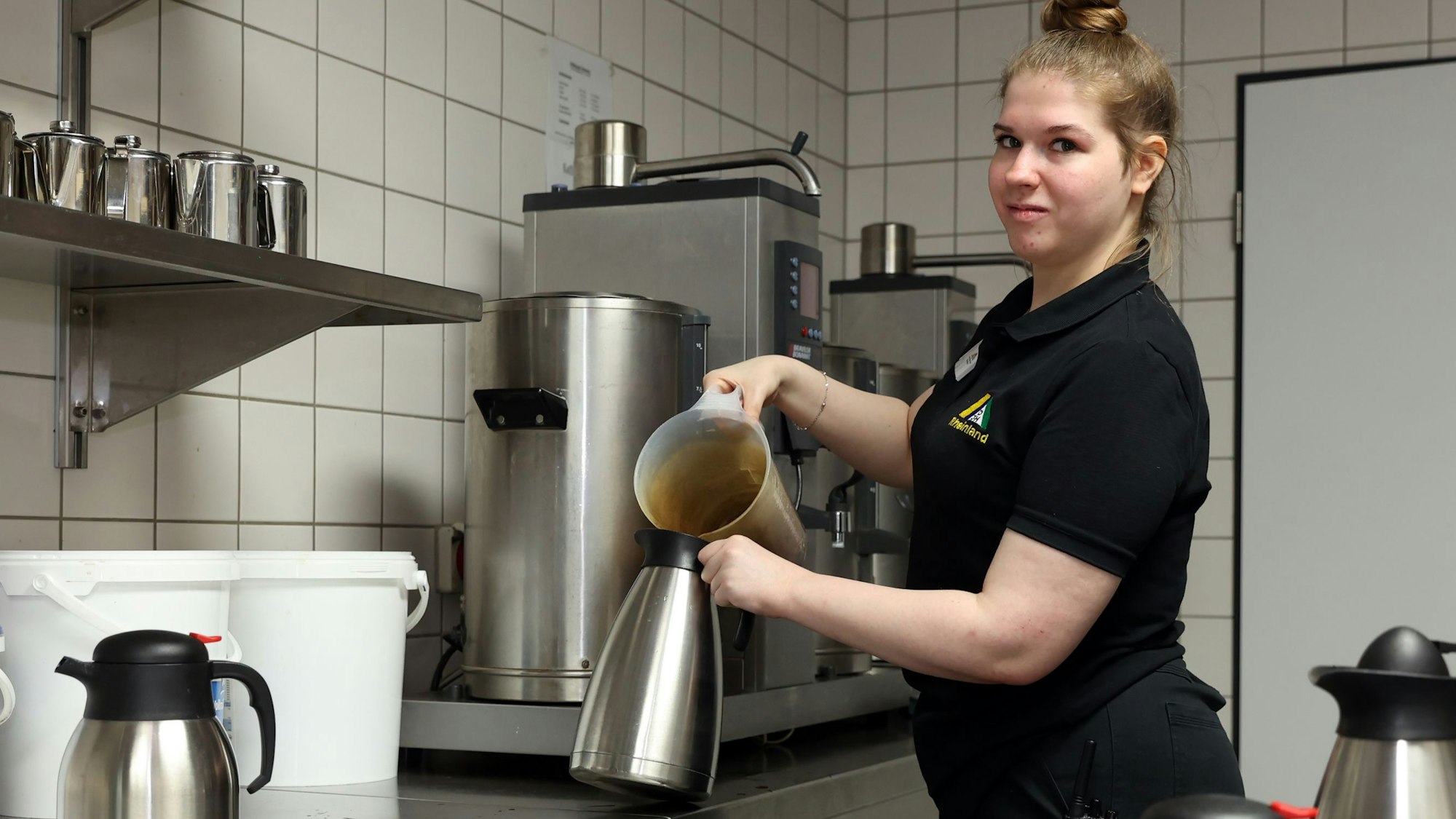 Eine junge Frau in Schwarz füllt Kaffee in eine silberne Kanne.