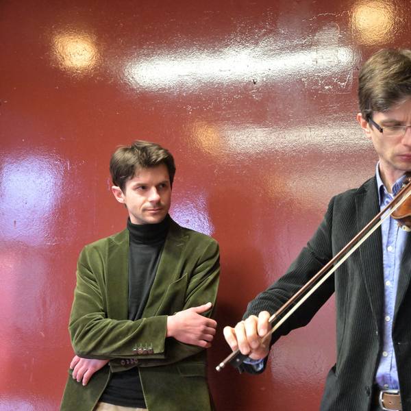 Roman Salyutov steht an einer Wand hinter Alexander Lifland, der auf der historischen Geige spielt.