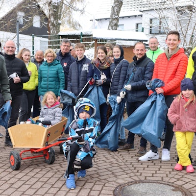 Eine Gruppe von Menschen hat sich versammelt, um Müll aufzusammeln. Sie haben blaue Müllsäcke und Zangen in der Hand.