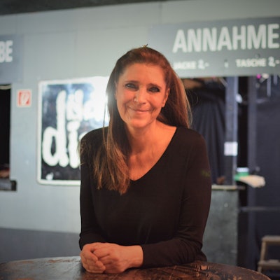 Claudia Wecker steht an einem Bartisch vor einer Wand mit dem Logo vom Club Das Ding.