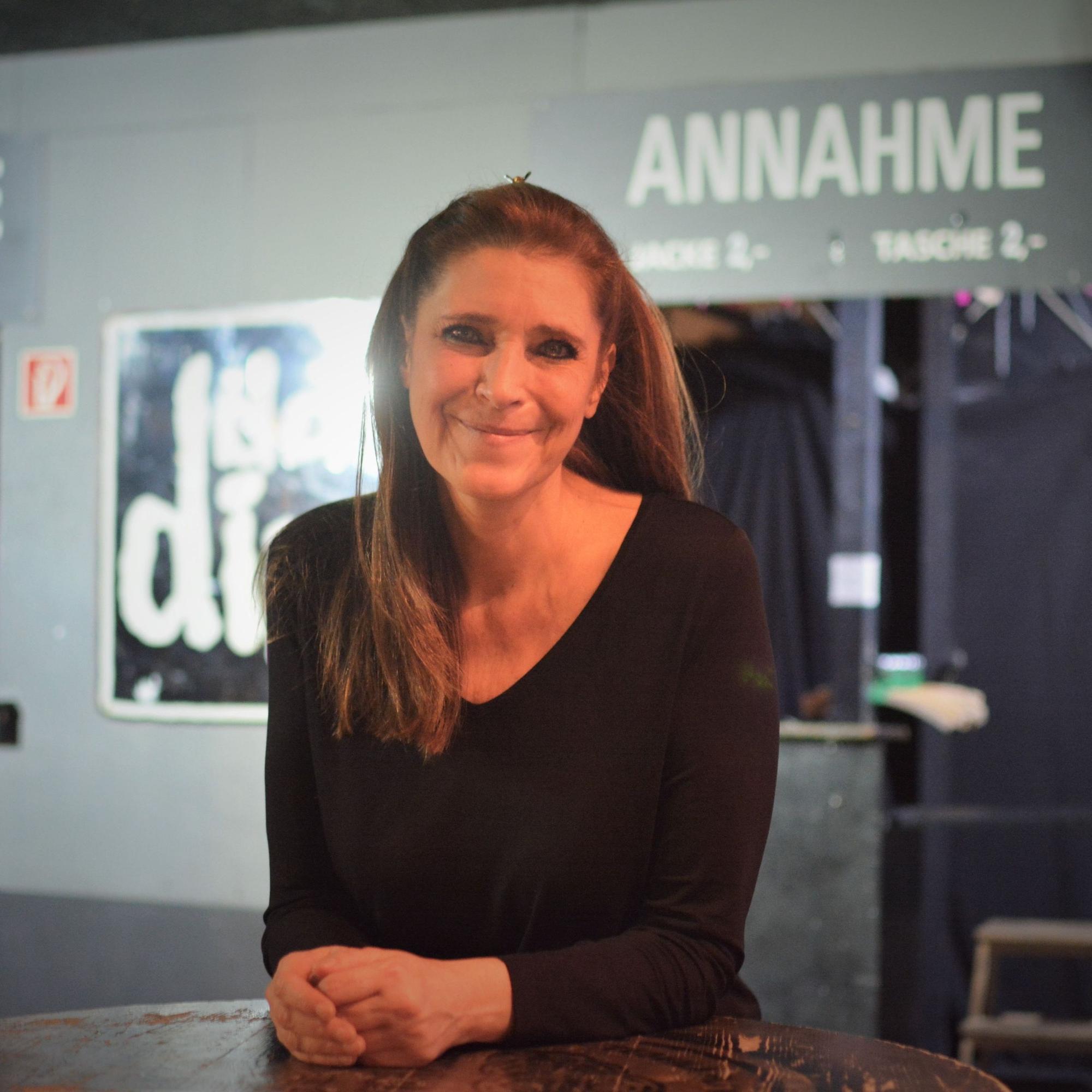 Claudia Wecker am Tisch in ihrem Club, im Hintergrund die Garderobe.