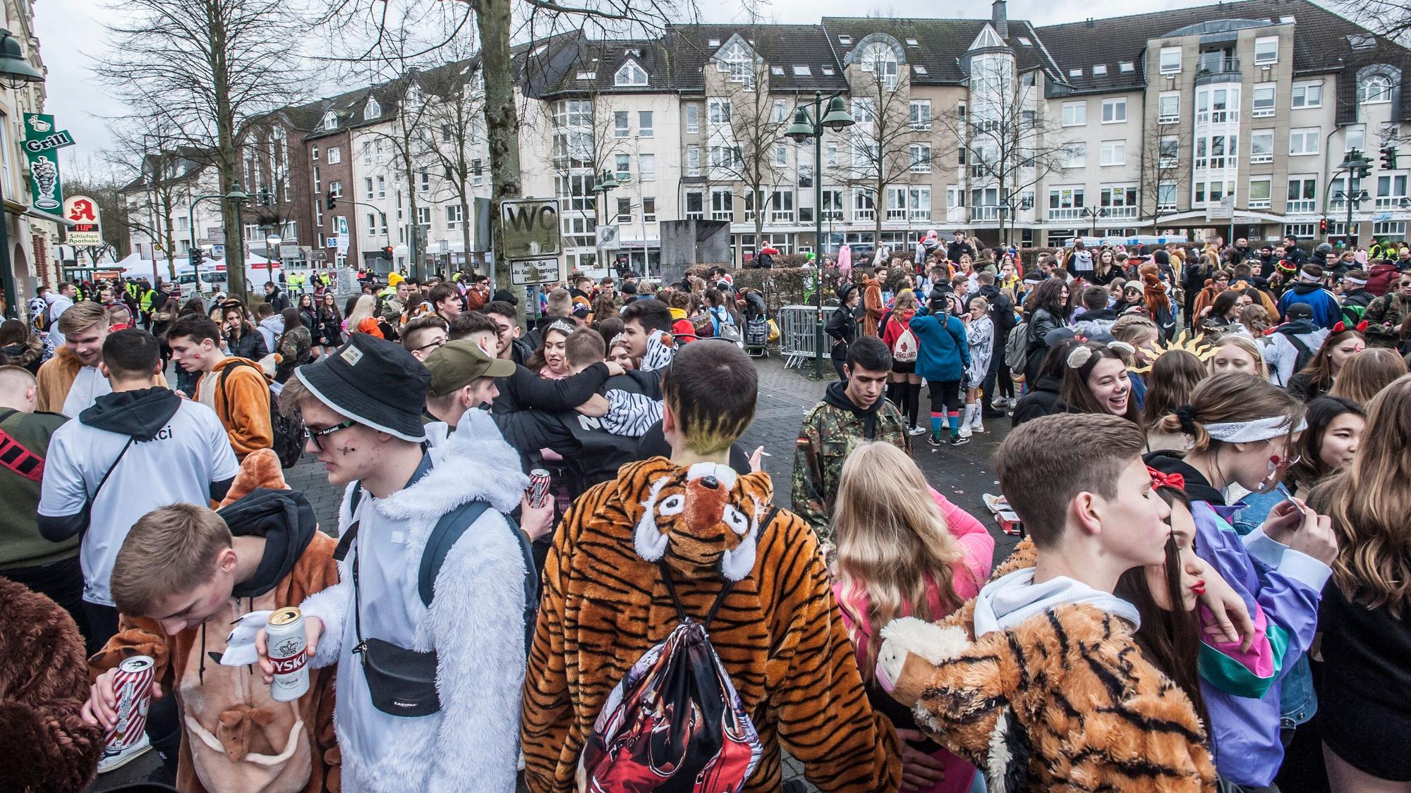 Hunderte Jugendliche stehen verkleidet an Karneval auf einem Platz. Es ist zu sehen, dass einige von ihnen Bierdosen in der Hand haben.