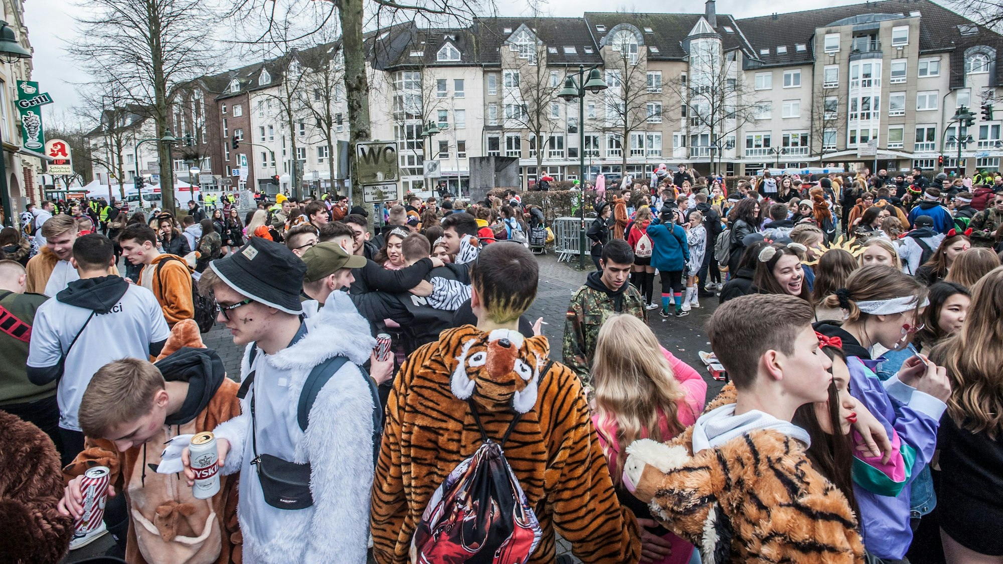 Hunderte Jugendliche stehen verkleidet an Karneval auf einem Platz. Es ist zu sehen, dass einige von ihnen Bierdosen in der Hand haben.