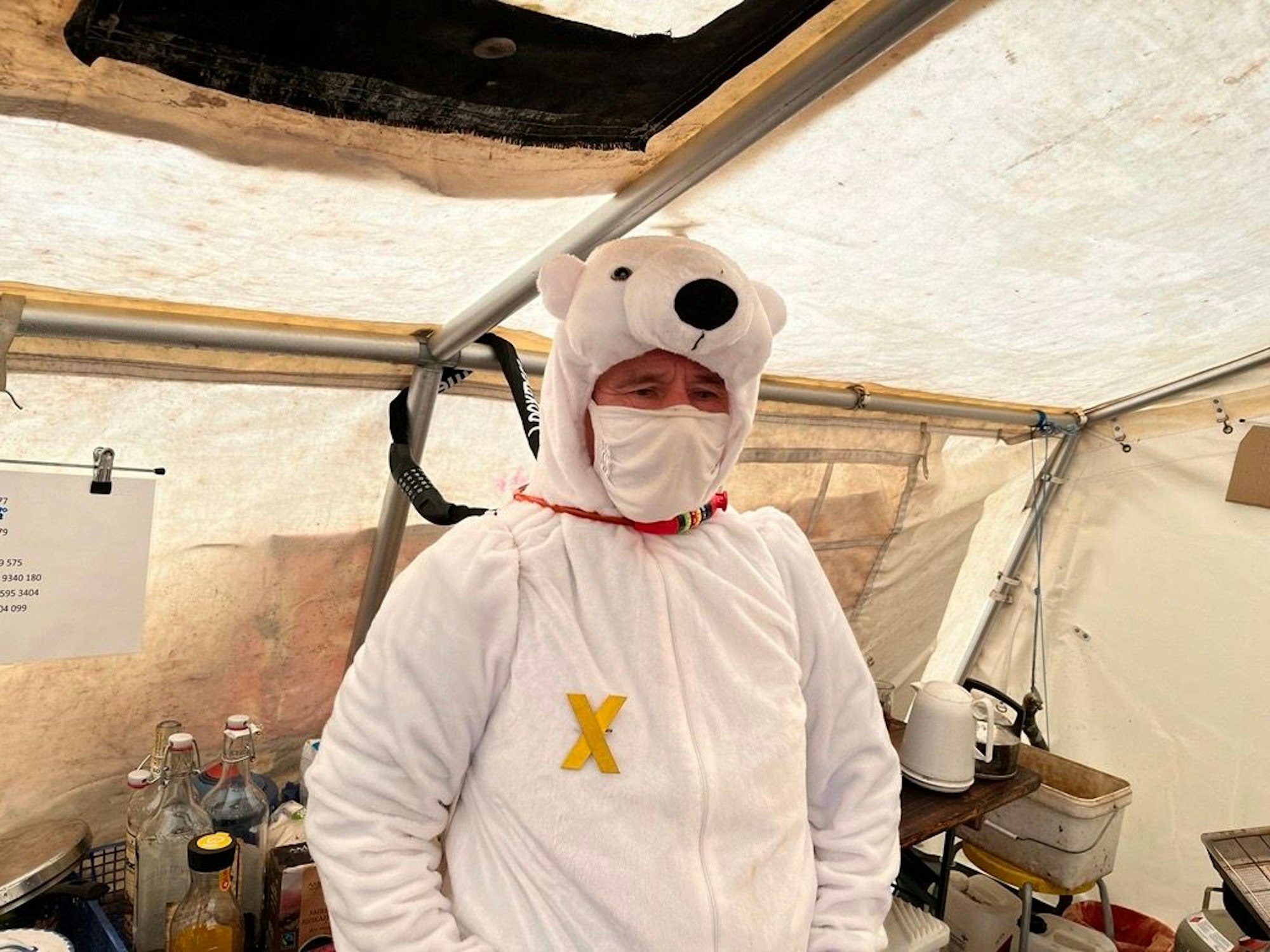Ein Mann hat sich als Eisbär verkleidet und an eine Zeltstange gekettet. Auf seiner Brust ist das gelbe Kreuz zu sehen, das die Besetzer von Lützerath auch am Ortseingang errichtet hatten.