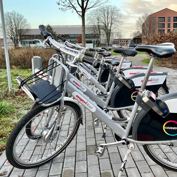 Mehrere Wupsi-Leihräder an der Mobilstation in der Neuen Bahnstadt Opladen, im Hintergrund die Technische Hochschule
