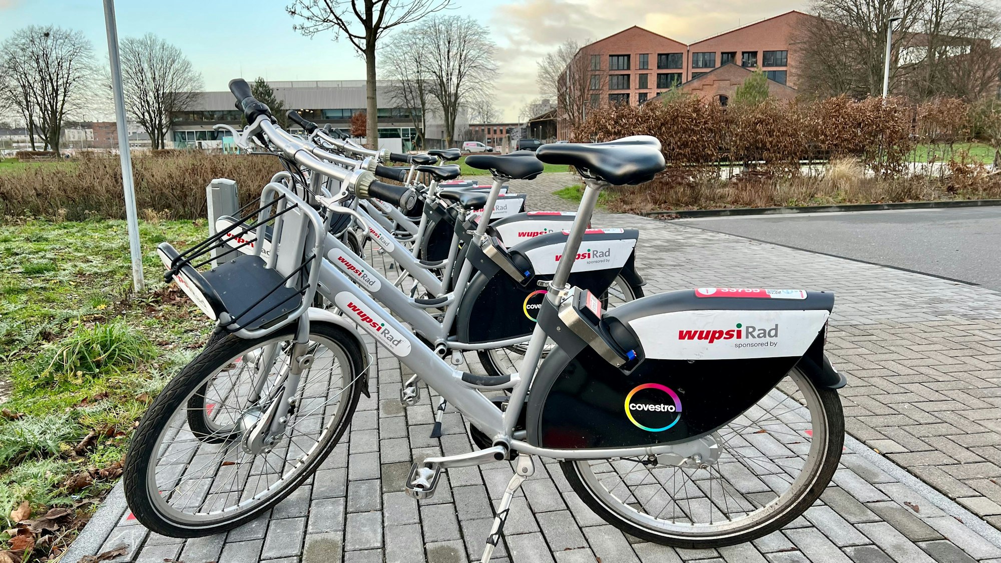 Mehrere Wupsi-Leihräder an der Mobilstation in der Neuen Bahnstadt Opladen, im Hintergrund die Technische Hochschule
