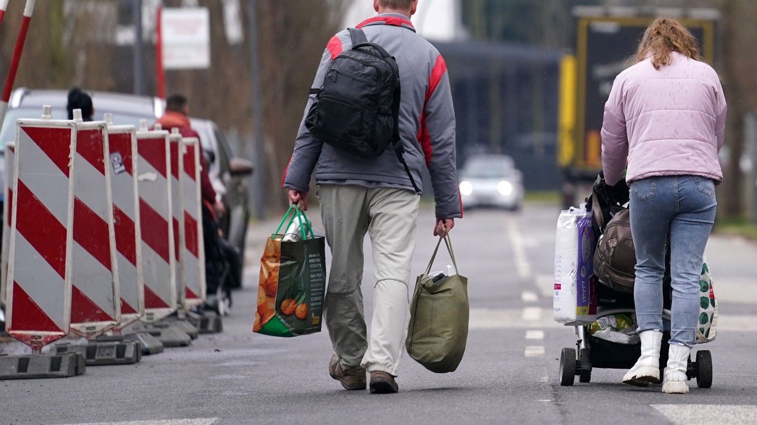 Ein aus der Ukraine geflüchteter Mann und eine Frau mit Kinderwagen verlassen mit Gepäck eine Flüchtlingsunterkunft.