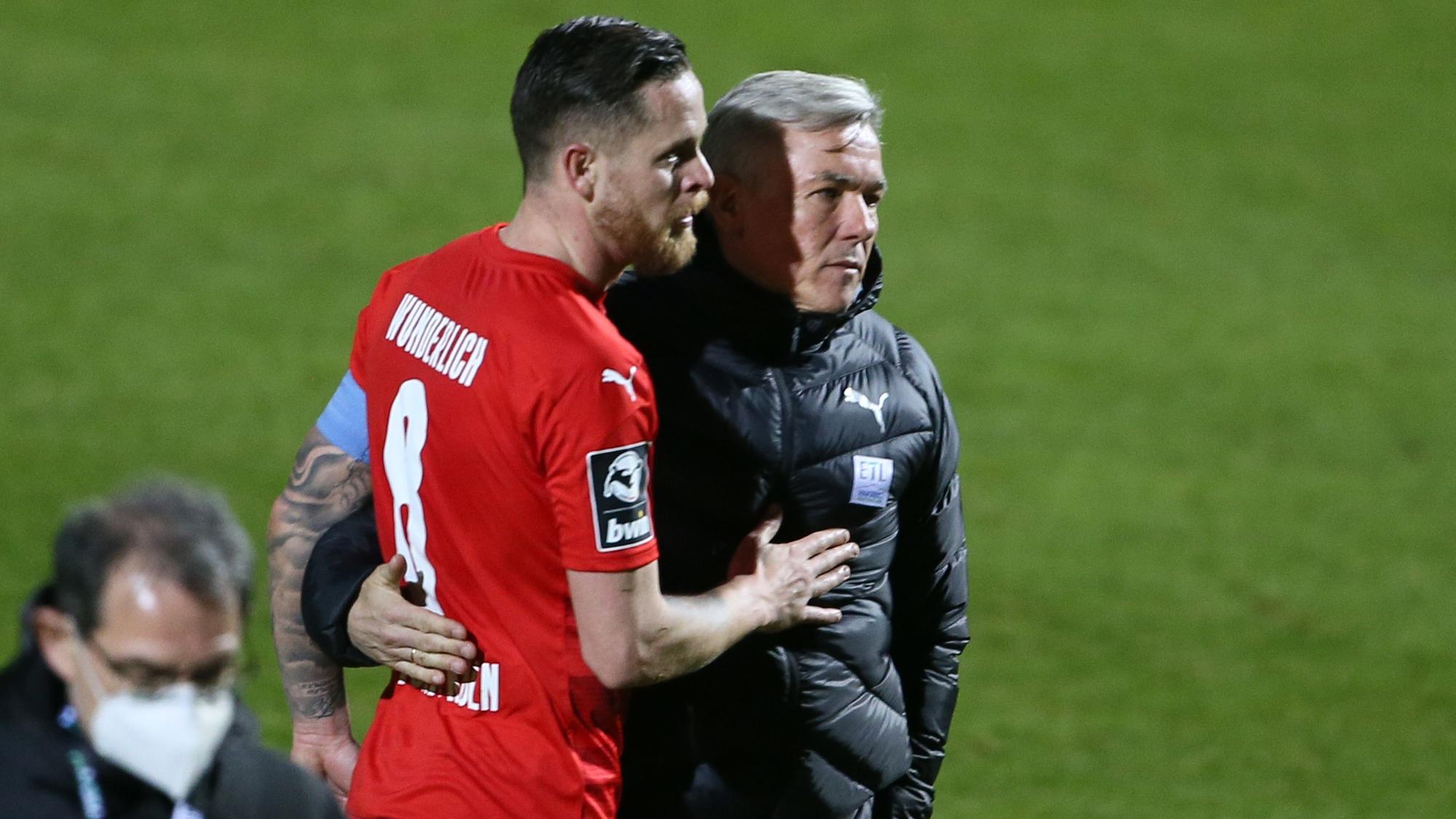 Ein Fußballtrainer nimmt seinen Kapitän nach Spielschluss in den Arm.