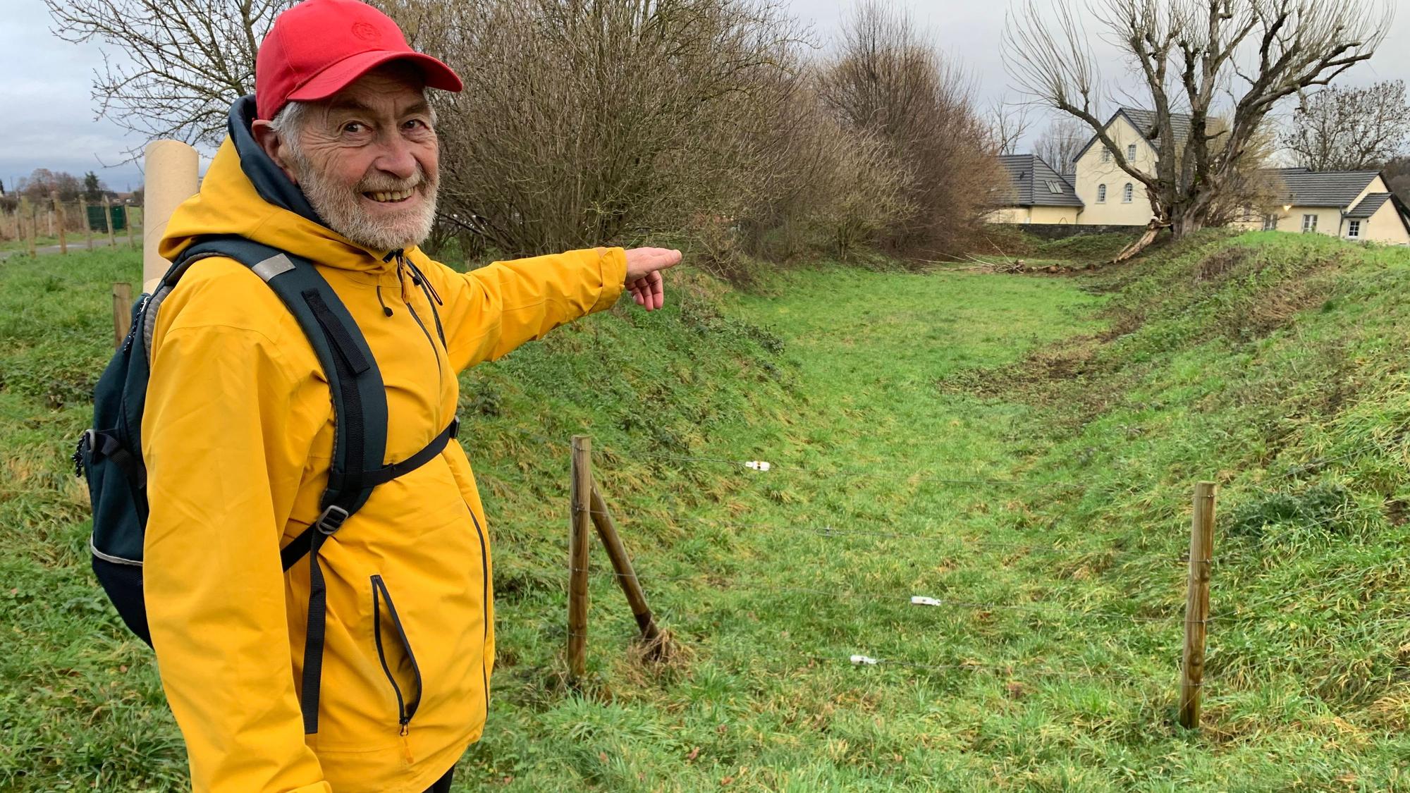 Ein älterer Herr in gelber Regenjacke zeigt auf einen ausgetrockneten Mühlengraben.