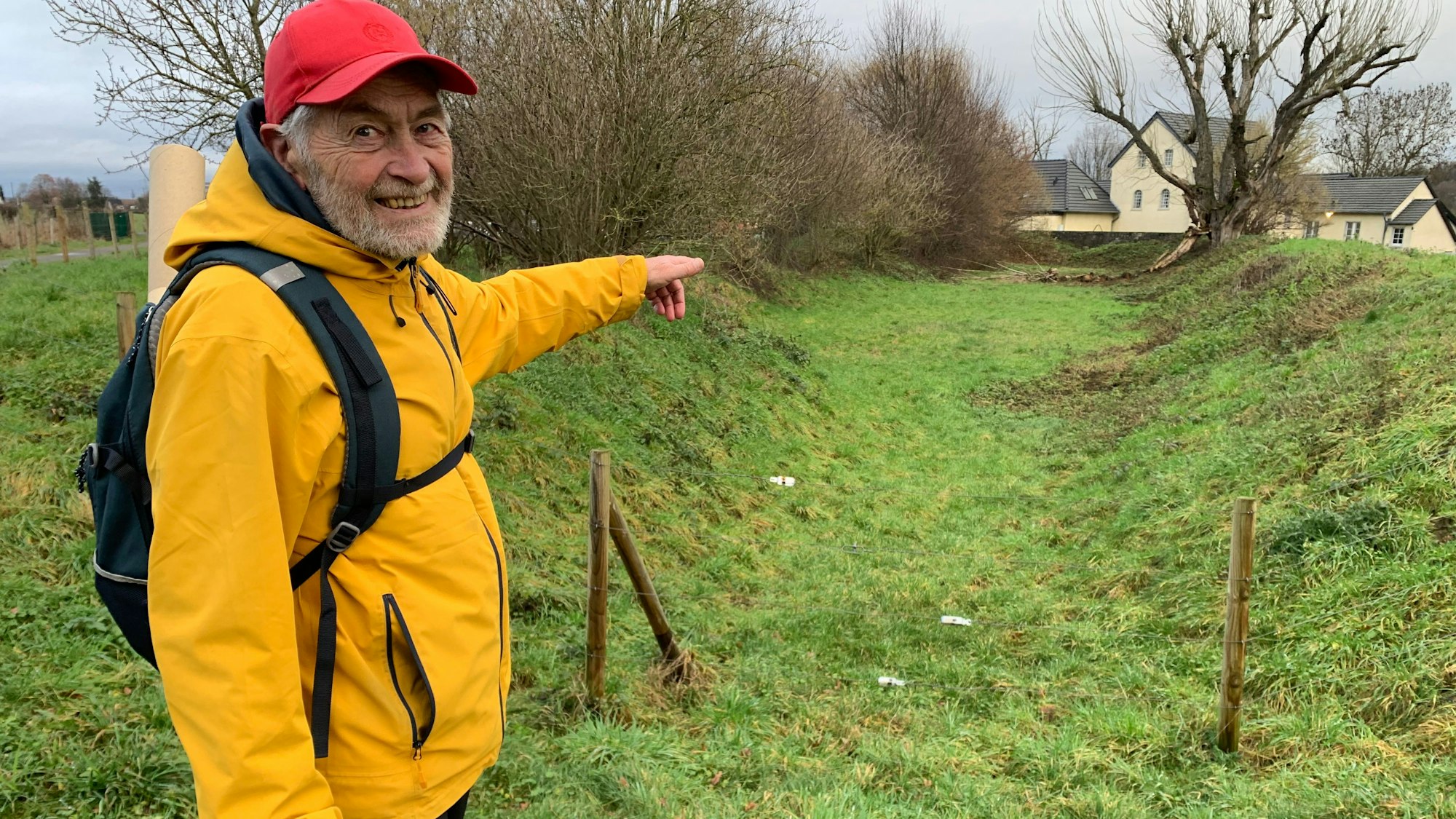 Ein älterer Herr in gelber Regenjacke zeigt auf einen ausgetrockneten Mühlengraben.