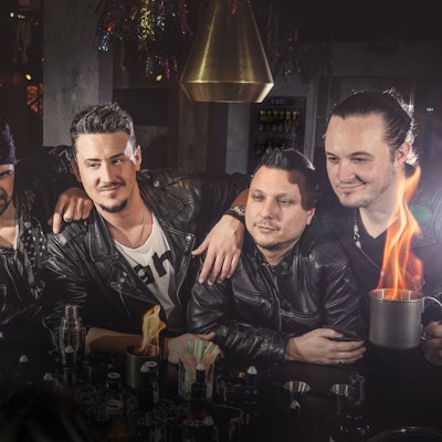 Fünf Musiker stehen an einer Theke und haben brennende Drinks vor sich stehen.