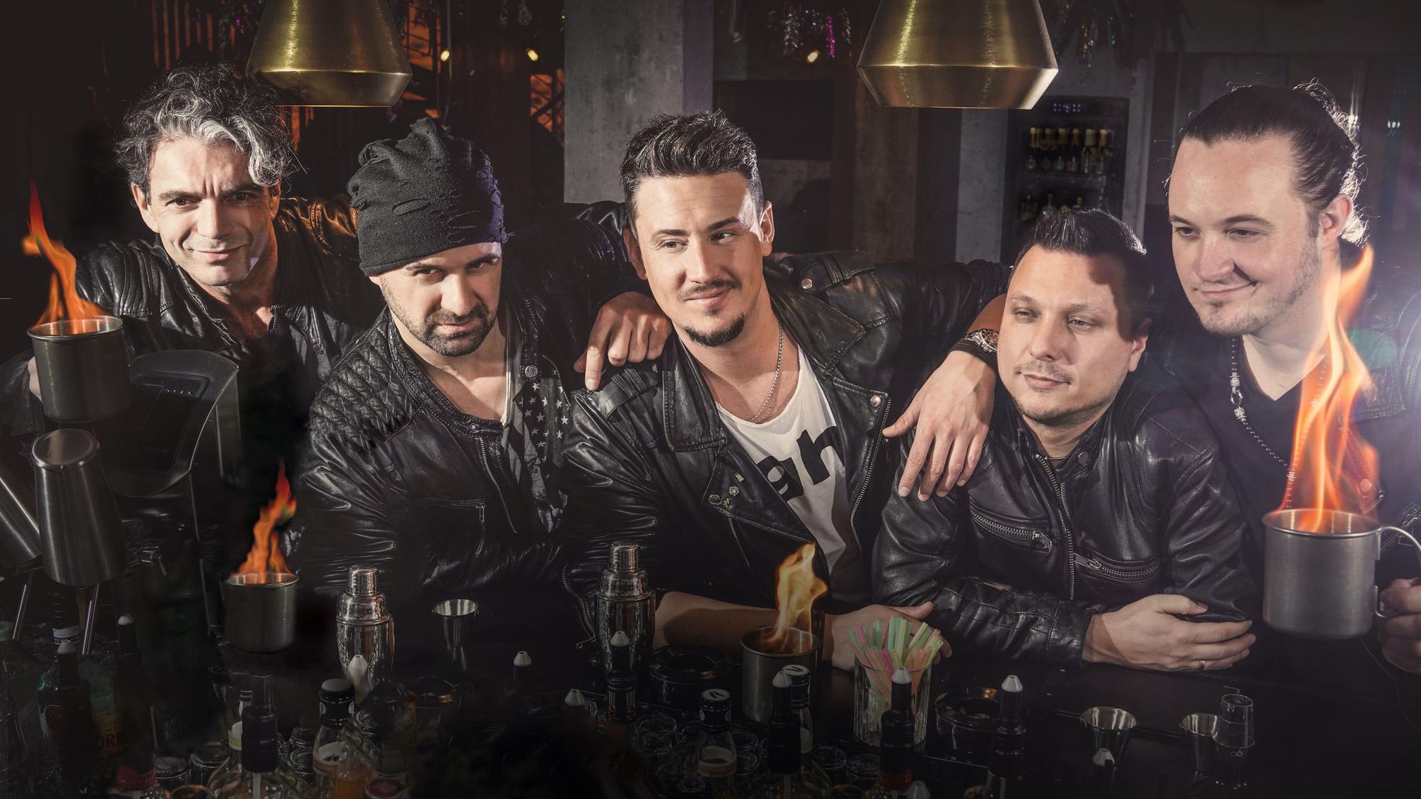 Fünf Musiker stehen an einer Theke und haben brennende Drinks vor sich stehen.