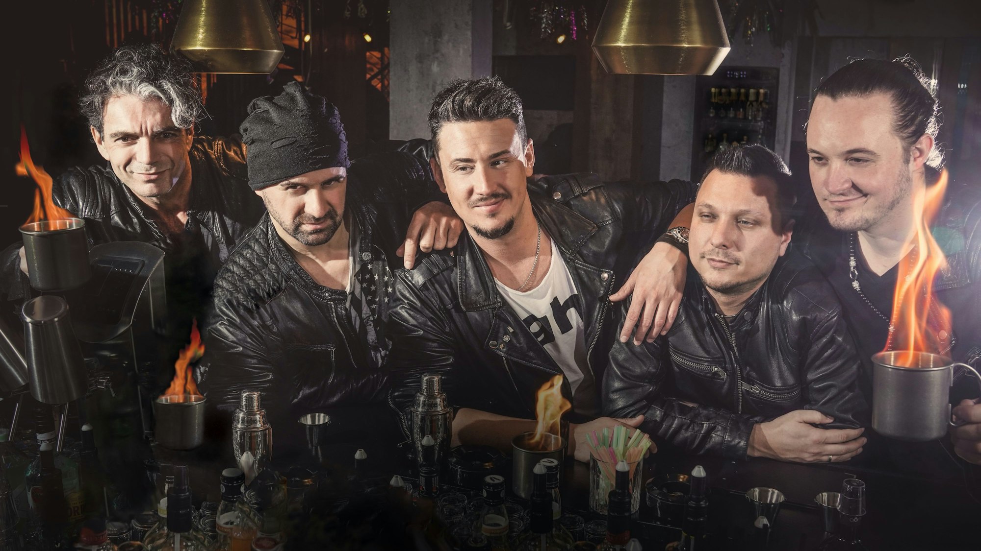 Fünf Musiker stehen an einer Theke und haben brennende Drinks vor sich stehen.