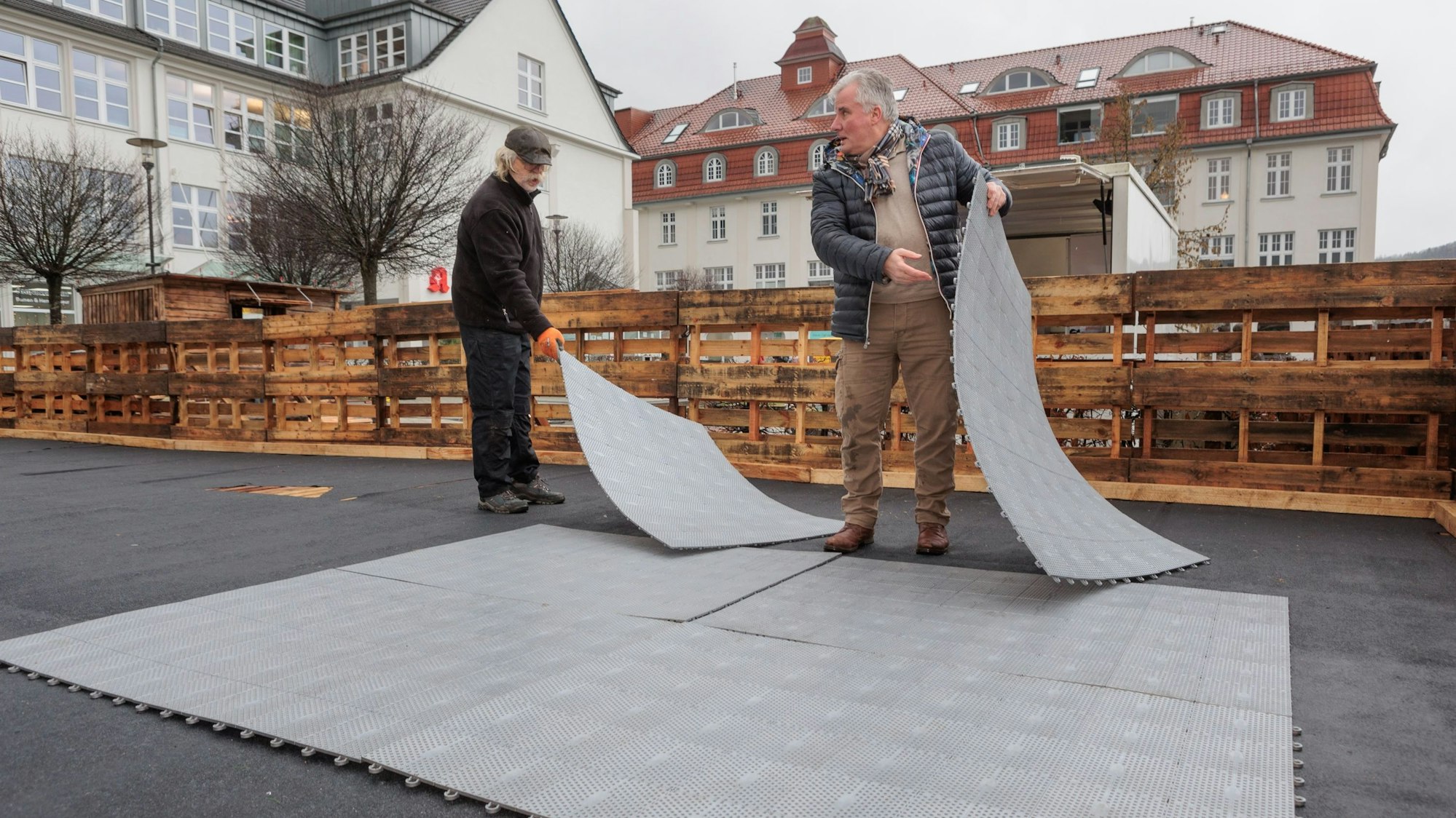 Zwei Männer bauen eine Kunststoffbahn aus mehreren Matten auf.