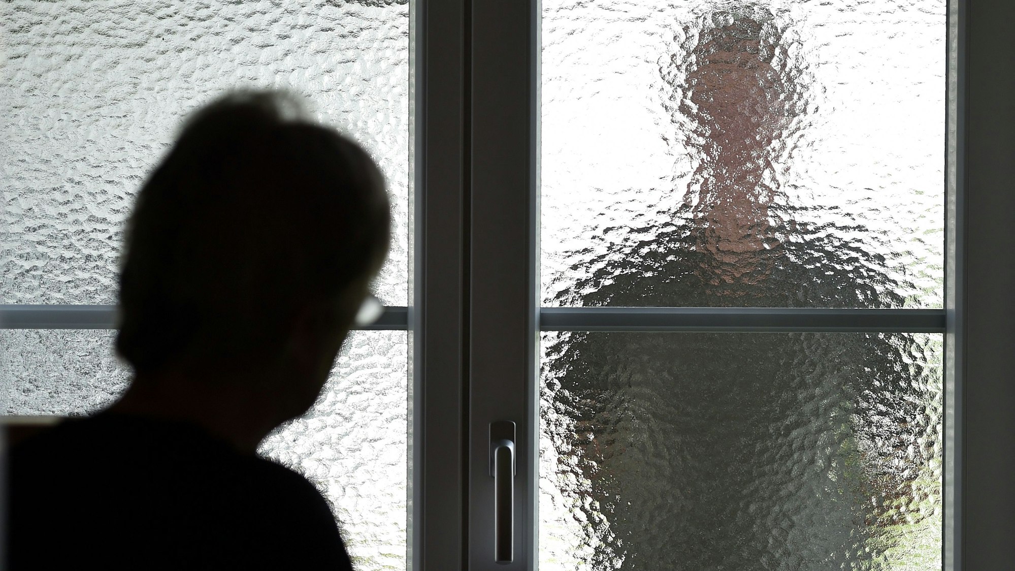 Eine Frau steht an einer Glasscheibe, hinter der ein Stalker steht. (gestellte Szene)