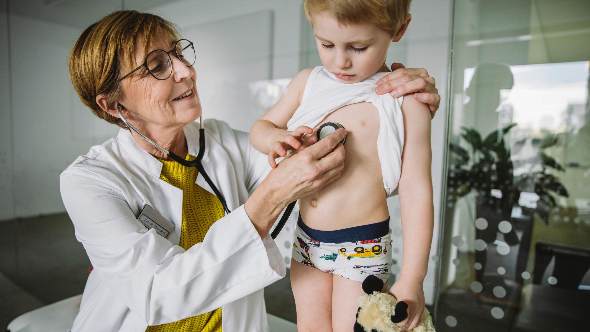Eine Kinderärztin untersucht einen kleinen Jungen mit dem Stethoskop.