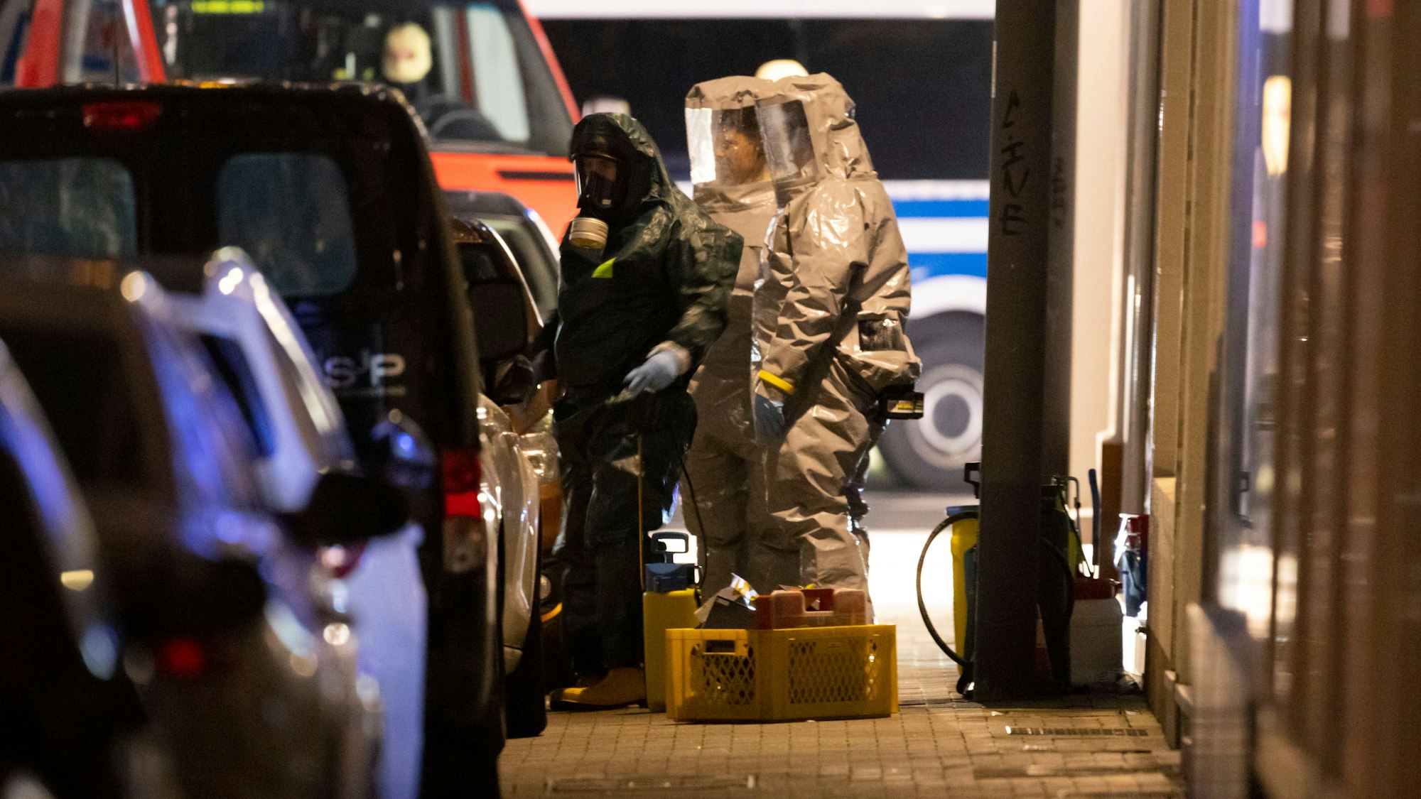Einsatzkräfte in Schutzmontur und mit Atemmasken stehen auf dem Bürgersteig in Castrop-Rauxel neben Einsatzwagen.