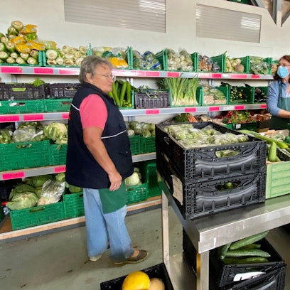 Margret Welsch und Helmi Dreifke sortieren Lebensmittel in der Euskirchener Tafel. Im Hintergrund sind prall gefüllte Regale mit Lebensmittelkisten zu sehen.
