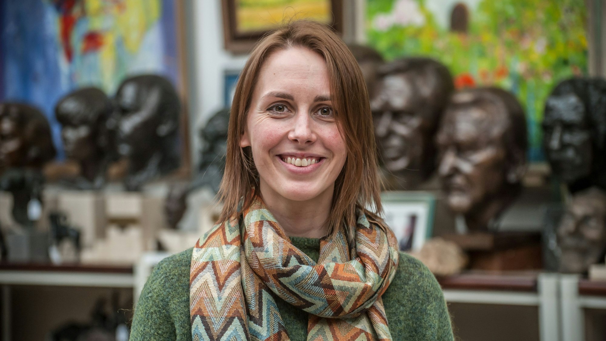 Die Autorin Anna Hanrahan lächelt in die Kamera, im Hintergrund sind etwa ein Dutzend bronzene Porträtbüsten zu erkennen.