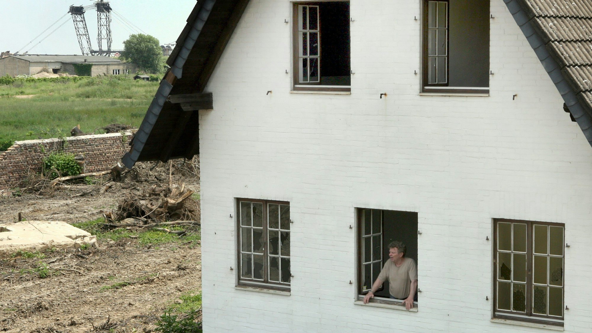 Ein Mann schaut am Freitag (16.06.2006) aus einem verlassenen Haus in Otzenrath (Kreis Jüchen), im Hintergrund ist der nahende Braunkohlebagger zu sehen.
