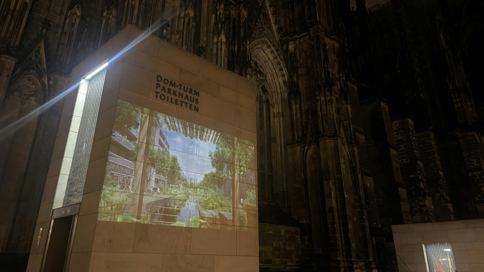 An einer Wand vor dem Kölner Dom wird eine Illustration projiziert. Darauf zu sehe ist eine grüne Stadt ohne Autos. Die Installation ist Teil des Projekts "Strassen befreien" einer Berliner Gruppe.