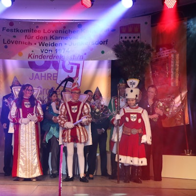 Vier Kinder in rot-weißen Karnevalstrachten stehen auf der Bühne. Hinter ihnen sind noch einige Erwachsene im Kostüm zu sehen.
