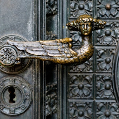 Das Bild zeigt einen bronzenen Türgriff in Form eines Engels mit Lockenkopf am Kölner Dom.