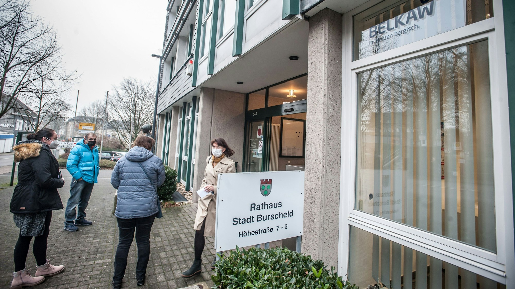 Besucher des Burscheider Rathauses stehen vor dem Gebäude und tragen Mund-Nasen-Schutzmasken.