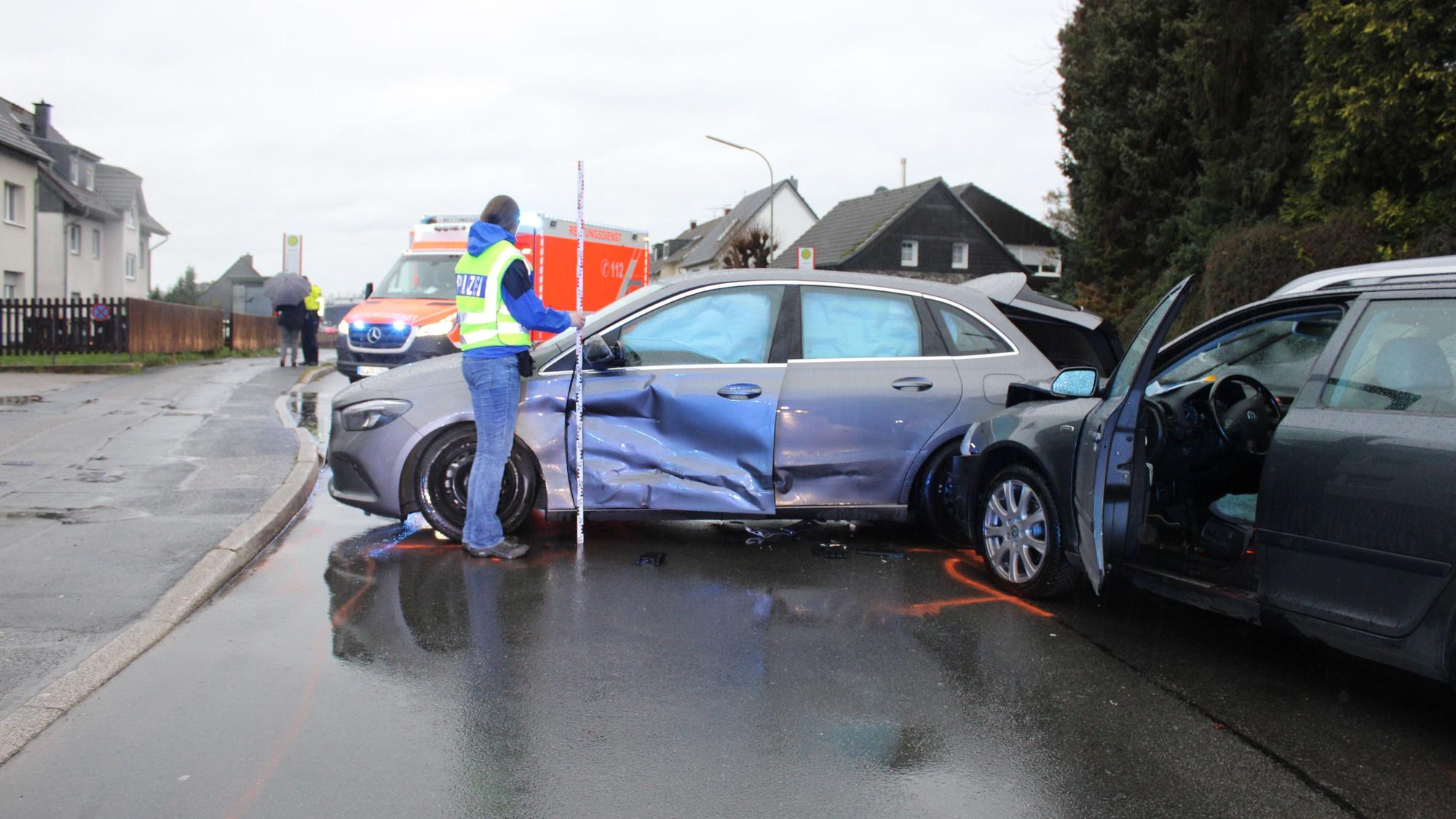 Am Unfallort stehen die beiden aufeinandergeprallten Autos, eine Polizistin ist vor Ort, im Hintergrund ein Rettungswagen.