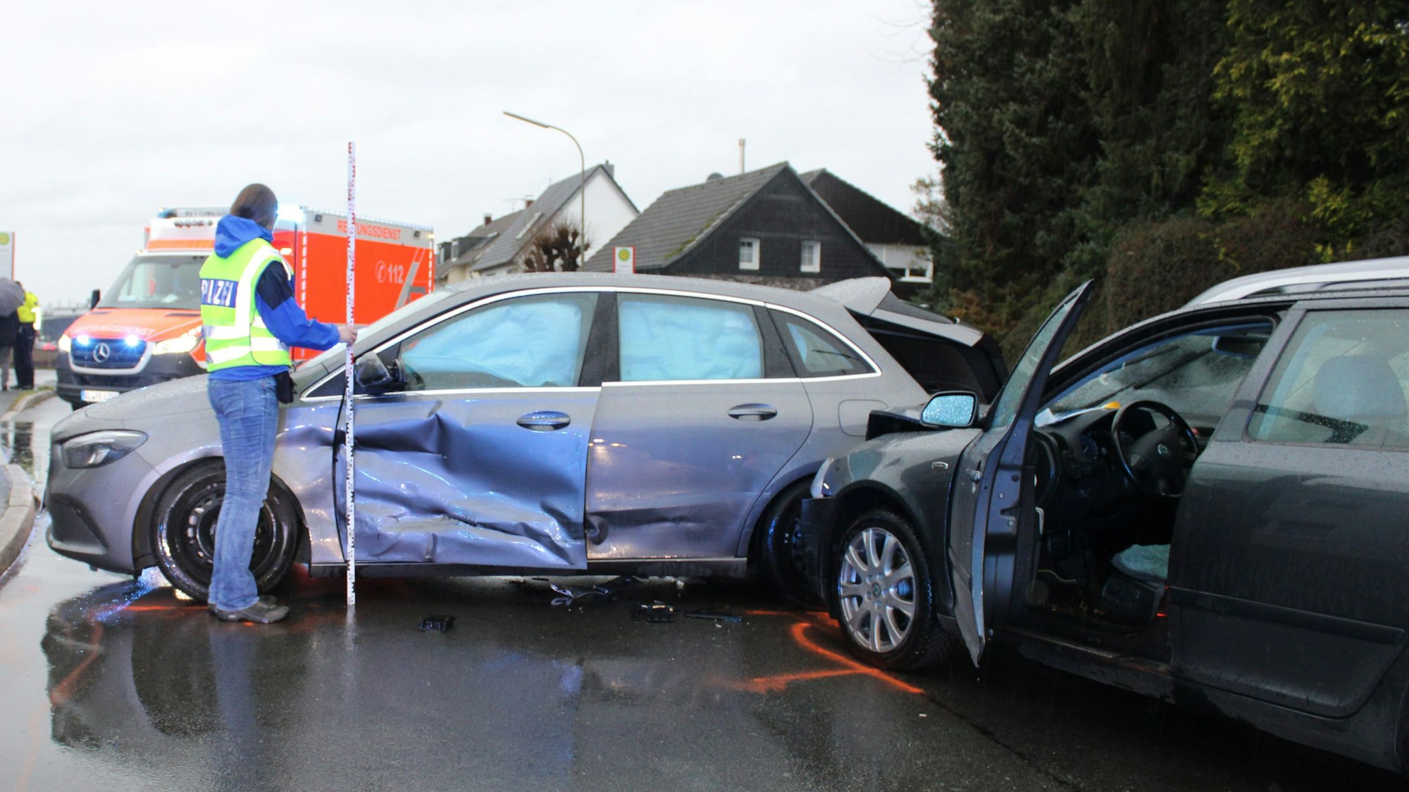 Eine Polizeibeamtin hält einen Maßstab an ein Unfallauto, das mit einem weiteren zusammengestoßen ist.