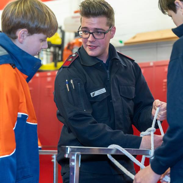 Das Foto zeigt, wie Christian Lipphold, Feuerwehrmann bei der freiwilligen Feuerwehr Porz-Langel, Kindern das Knoten von Seilen beibringt.