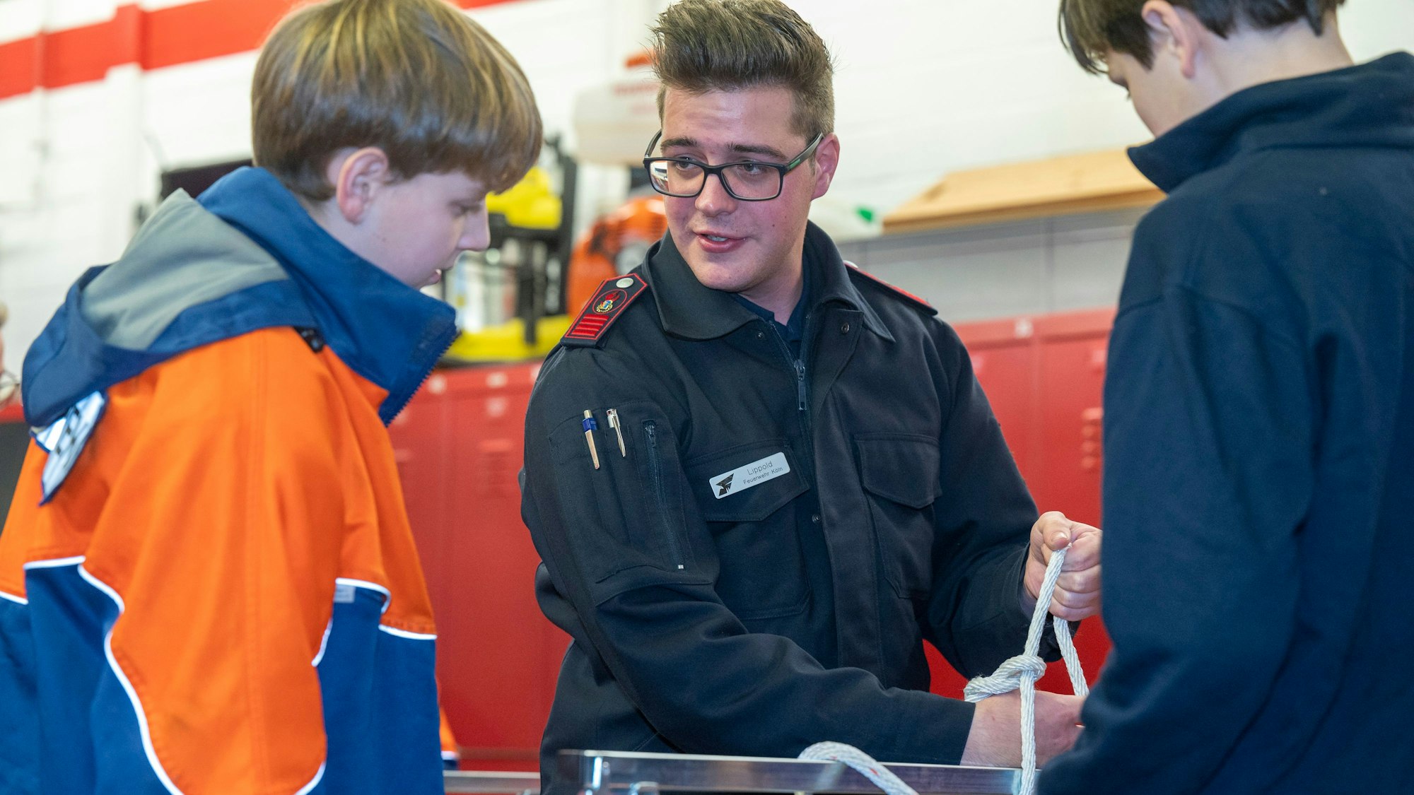 Das Foto zeigt, wie Christian Lipphold, Feuerwehrmann bei der freiwilligen Feuerwehr Porz-Langel, Kindern das Knoten von Seilen beibringt.