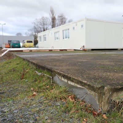 Auf einer großen Bodenplatte steht ein weißer Wohncontainer.